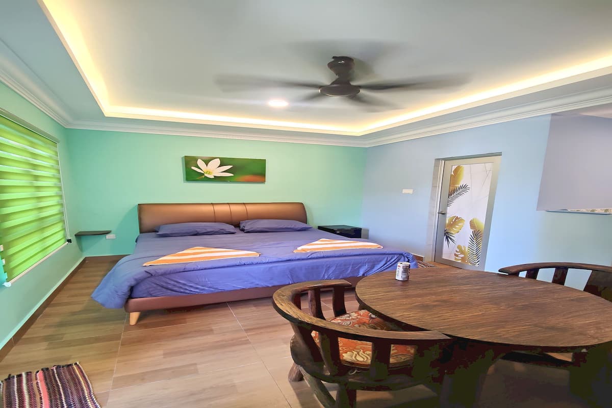 A bedroom with a bed, a ceiling fan, a table with chairs, and a door with a leaf-patterned design.