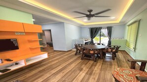 A dining area with a round wooden table and chairs, a ceiling fan, and a television on an orange stand. - Capital O 90949 Pelangi Beach Resort Mersing (Langkawi)