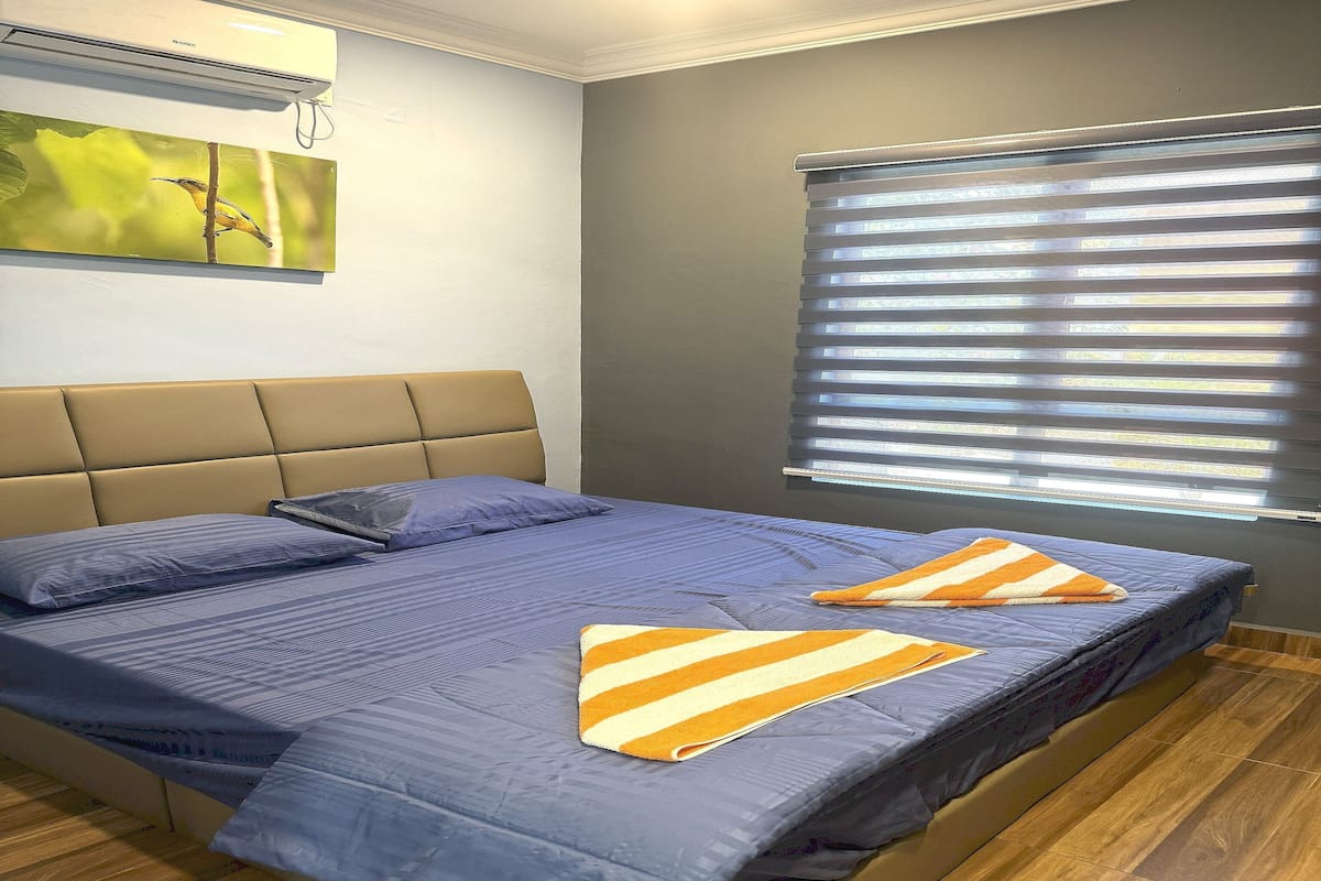 A bedroom with a bed, a window with blinds, and a wall-mounted air conditioner.