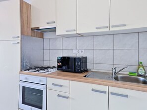 A modern kitchen with a gas stove, a microwave, a sink, and white cabinets. - Nice apartment for 4 people with WIFI, A/C, TV and terrace (Zadar)