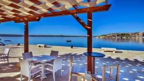 An outdoor seating area with tables and chairs, a pergola structure, and a view of a calm body of water with a boat. - Lovely apartment for 4 people with A/C, WIFI, TV and terrace (Zadar)