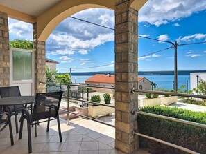 Un balcon avec une table et des chaises, un pilier en pierre et une vue sur la mer et les bâtiments.