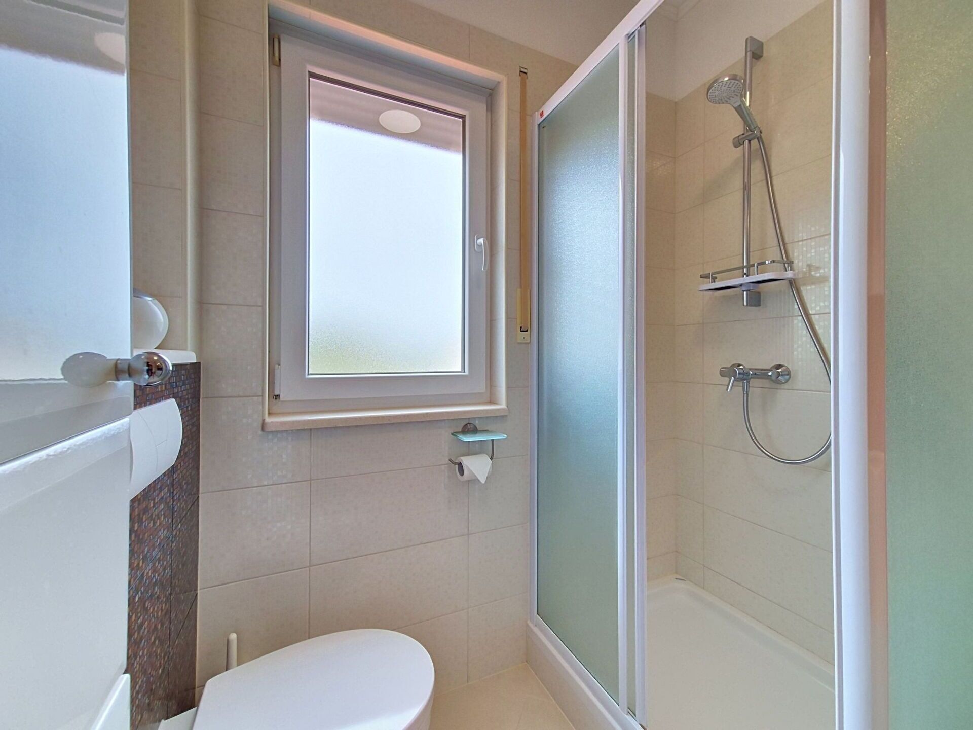 A bathroom with a toilet, a window, and a shower area.