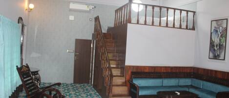 Une pièce avec un escalier en bois, un canapé bleu, un fauteuil à bascule et un revêtement de sol à motifs.