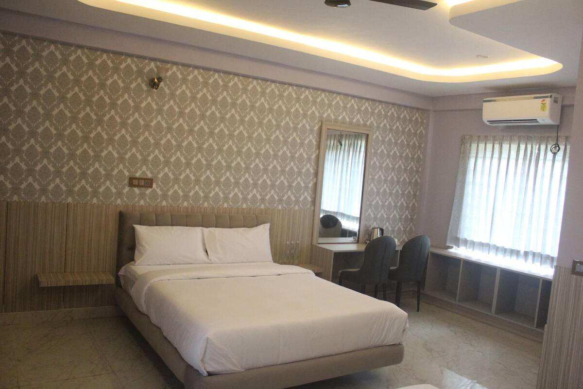 Una habitación de hotel con cama, escritorio, silla, espejo y aire acondicionado.