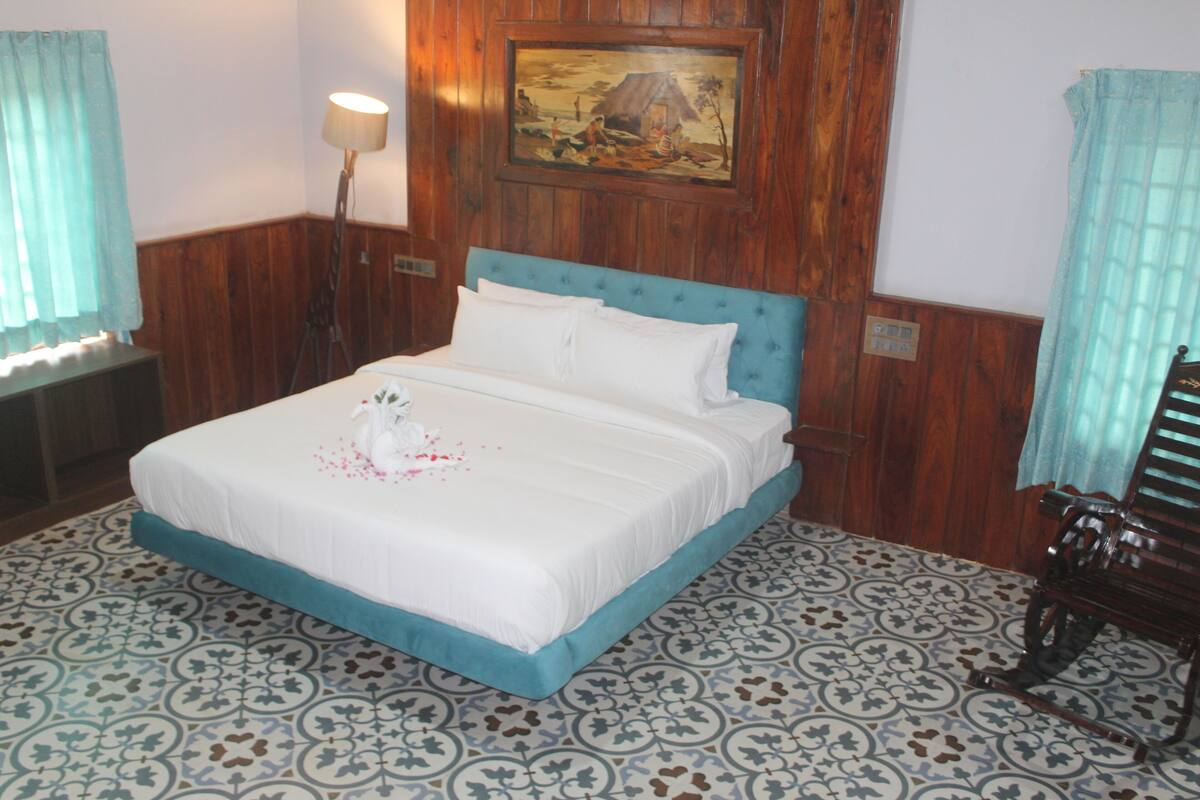 Una cama bien hecha con sábanas blancas y un cabecero azul, un cuadro en la pared y baldosas de suelo estampadas.
