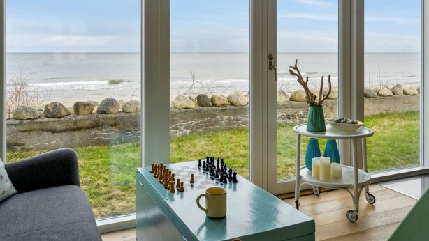 Une pièce avec un jeu d’échecs, une tasse et une vue sur la plage, visible à travers de grandes fenêtres.
