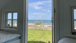 Une pièce avec un lit, une fenêtre et une porte donnant sur un espace verdoyant avec vue sur l’océan.