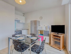 Cocina compacta con comedor, microondas, refrigerador, televisor y un reloj en la pared.
