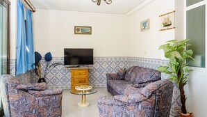 Una sala de estar con sofás estampados, una mesa de centro de vidrio, un televisor y una planta en maceta.