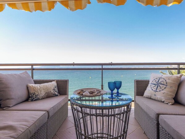 A balcony with wicker furniture, a glass table, and two blue glass cups.