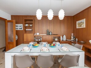A dining area with a glass-top table, four chairs, and a wooden cabinet with shelves.