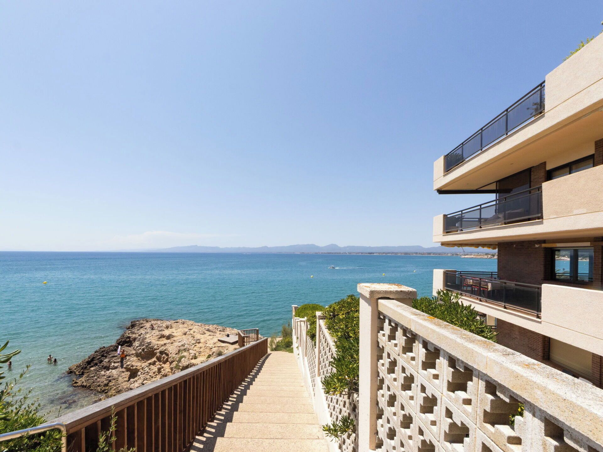 Ein Küstengebäude mit einem Balkon mit Blick auf das Meer, einen Felsen und einen klaren Himmel.