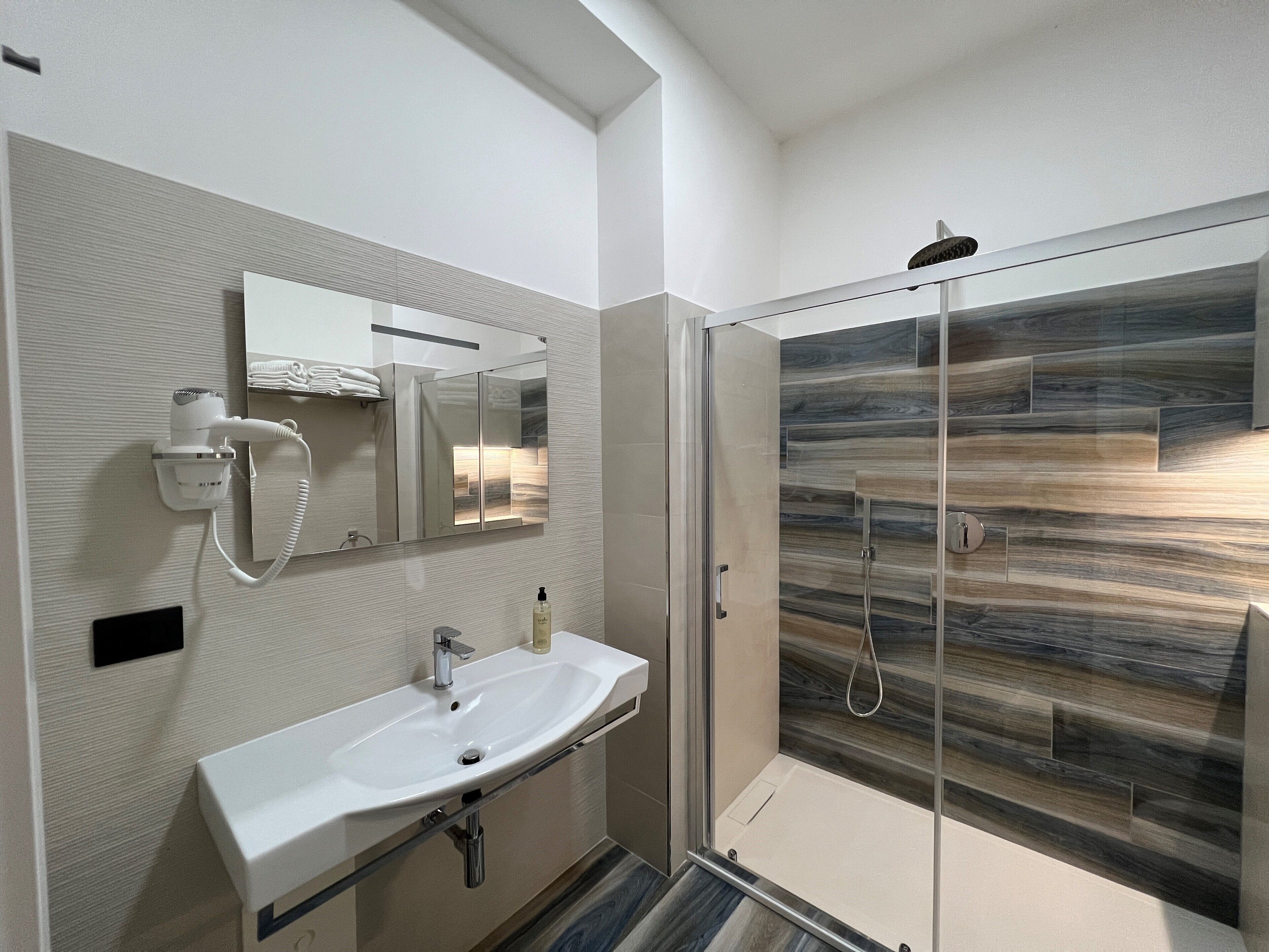 Une salle de bain moderne avec une douche à parois de verre, un lavabo blanc et un sèche-cheveux fixé au mur.