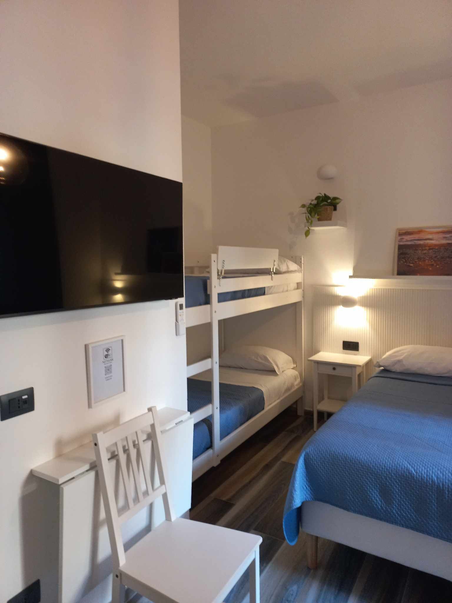 Una habitación con literas, un escritorio, una silla, una mesita de noche, una lámpara y un televisor.