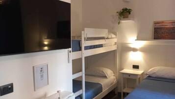 Una habitación con literas, un escritorio, una silla, una mesita de noche, una lámpara y un televisor.