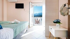 A bedroom with a bed, a TV, a sliding door to a balcony, and a small table with a vase. - Glikanisos House Nipos - Ideal for Hikers and Families 2bd, 6pl, 10min to Beach (Apokoronas)