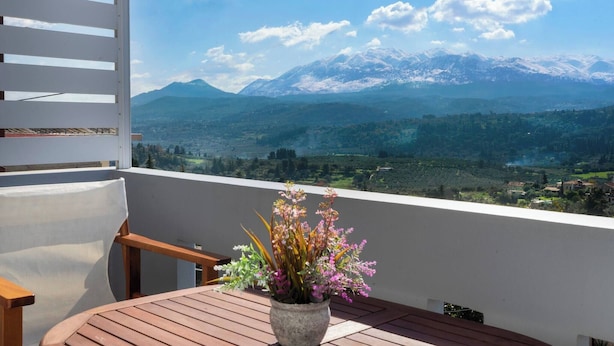 A balcony with a wooden table and a vase of flowers, overlooking a mountainous landscape. - Glikanisos House Nipos - Ideal for Hikers and Families 2bd, 6pl, 10min to Beach (Apokoronas)