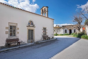 A building with a bell tower, a bench, and a mountain in the background. - Glikanisos House Nipos - Ideal for Hikers and Families 2bd, 6pl, 10min to Beach (Apokoronas)