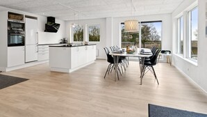 Eine moderne Küche mit weißen Schränken, einer zentralen Kochinsel und einem Essbereich mit rundem Tisch und Stühlen.