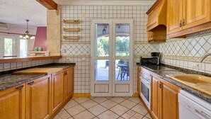 A kitchen with wooden cabinets, a tiled backsplash, a built-in oven, and a large window. - Stunning private villa for 6 people with WIFI, A/C, private pool, TV, terrace and pets allowed (Teulada)
