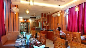A dining area with a long table set for a meal, wooden chairs, and a bar area in the background. - Hotel sunshine (Purnia)