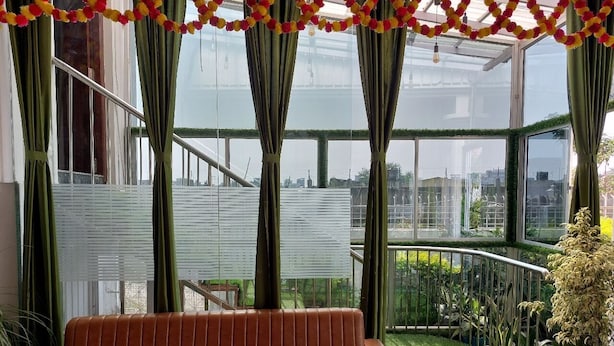 A conservatory with a leather sofa, green curtains, and a view of the cityscape. - Hotel sunshine (Purnia)