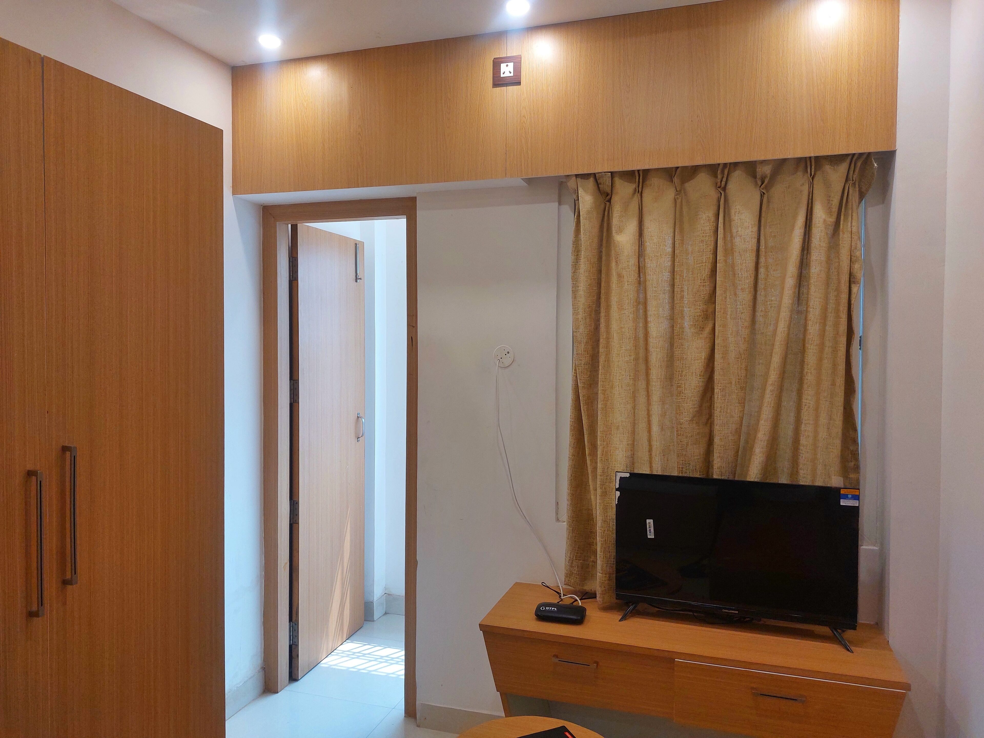 Une pièce avec une armoire en bois, un téléviseur posé sur un meuble en bois et un rideau.