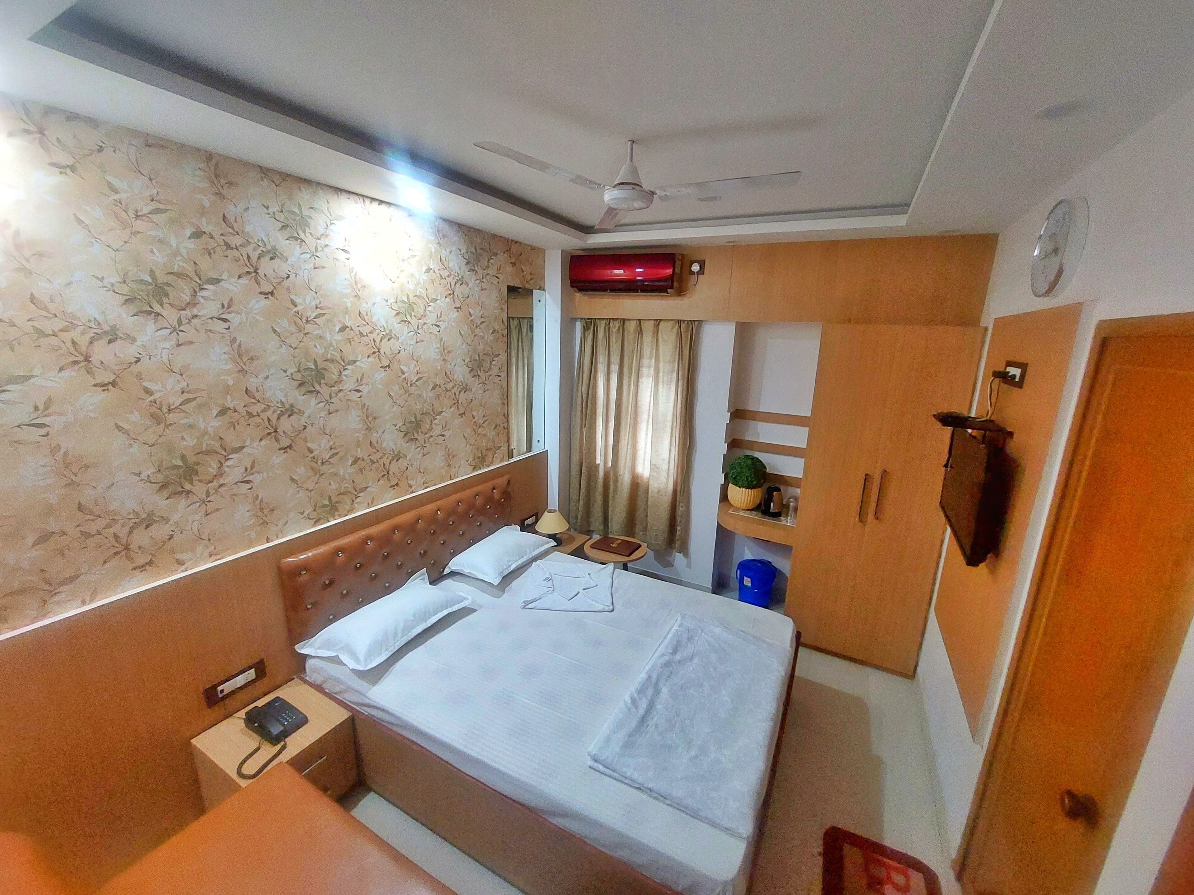 Habitación de hotel con cama, mesita de noche con teléfono, aire acondicionado de pared, ventilador de techo y reloj.