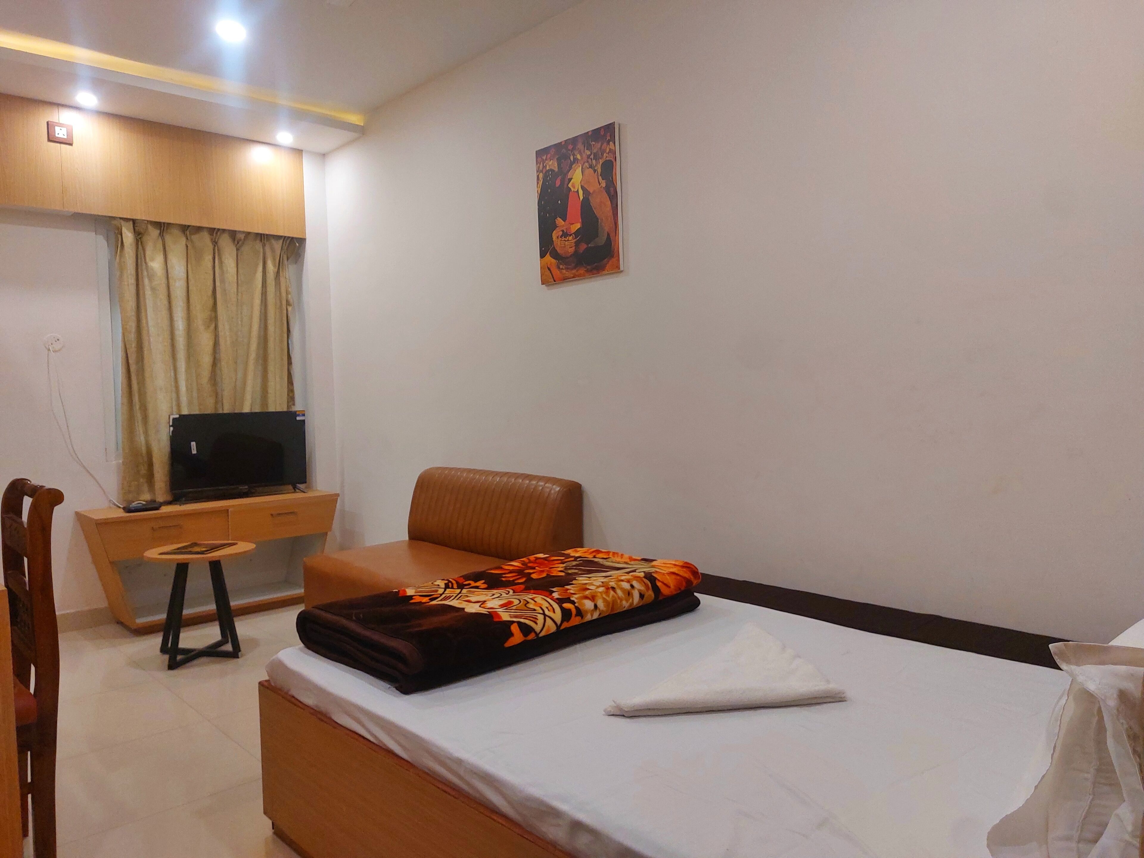 A hotel room with a bed, a desk with a computer, a chair, and a painting on the wall.