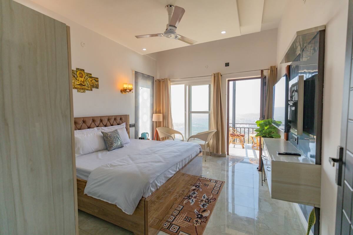 Un dormitorio amplio con una cama grande, ventilador de techo, balcón con vistas y televisor.