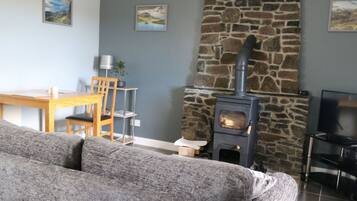 A living room with a stone fireplace, a wooden dining table, and a grey sofa.