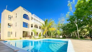 A modern building with a swimming pool, surrounded by greenery and trees. - Silent Palms Villa
 (diani)