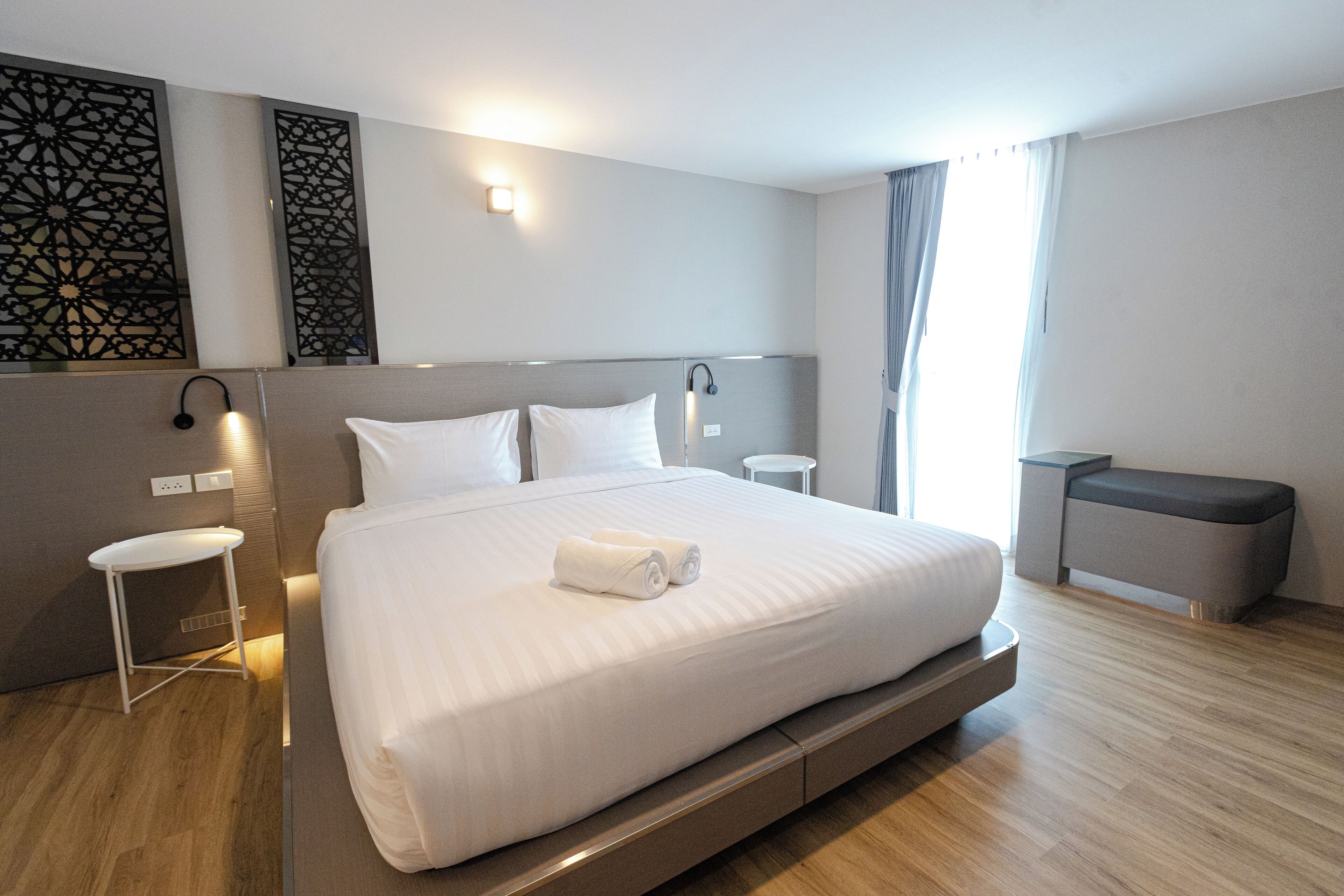 A modern hotel room with a large bed, bedside tables, a bench, and decorative wall panels.