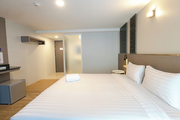 A hotel room with a large bed, a bedside table, a lamp, and a door leading to another room.