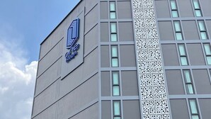 Un edificio moderno con un logotipo en la fachada, un acceso cubierto y un letrero que indica una altura máxima.