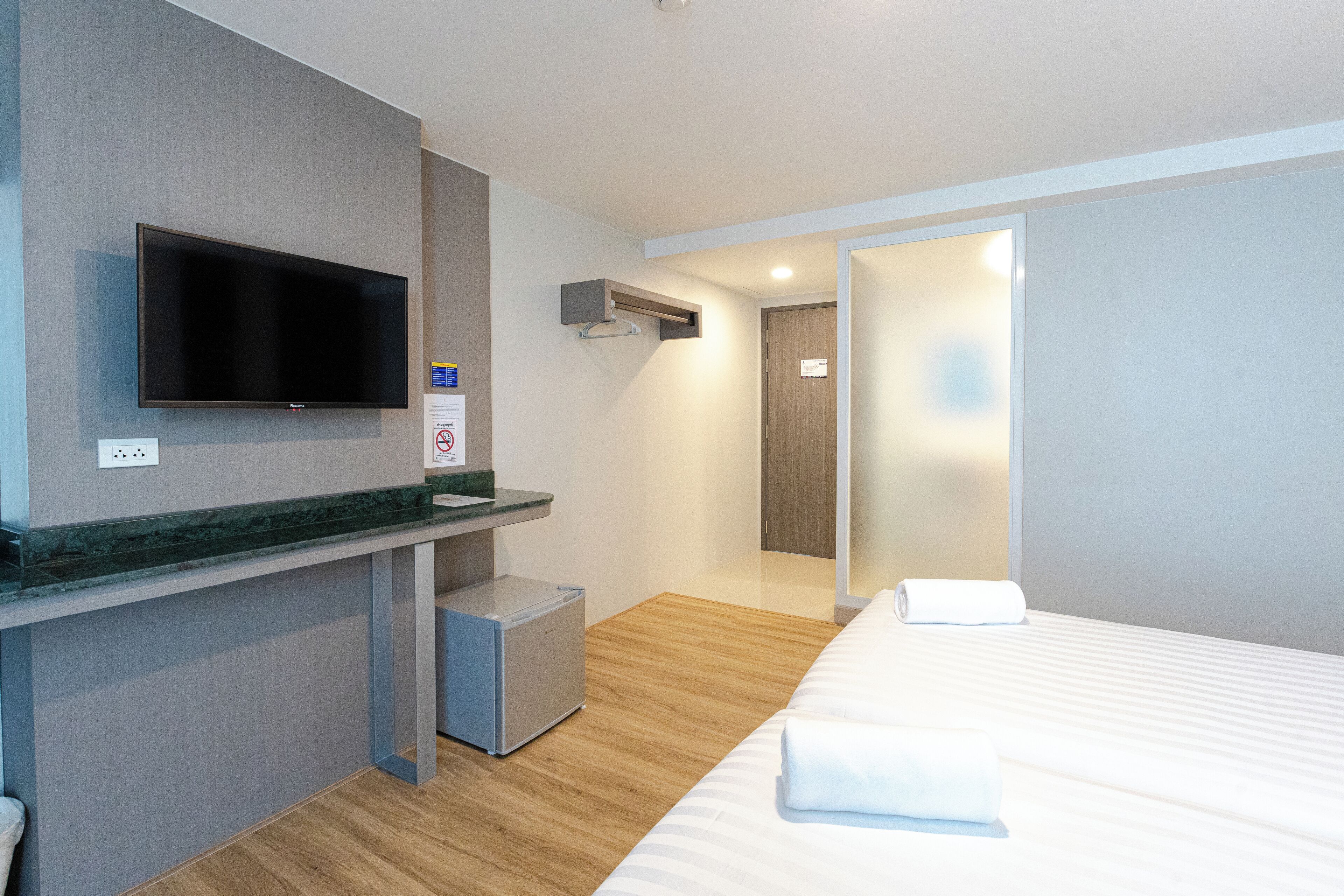 A hotel room with a bed, a TV mounted on the wall, a small refrigerator, and a wooden floor.
