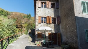 A stone building with wooden shutters, a patio with a table and chairs, and a small garden area. - Mansion in Pescaglia near Tuscan Coast (Pascoso - Pescaglia (LUCCA))
