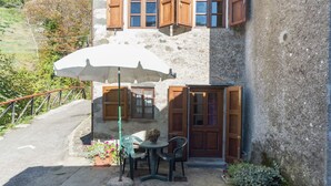 A stone building with wooden shutters and a small patio area with a table, chairs, and an umbrella. - Mansion in Pescaglia near Tuscan Coast (Pascoso - Pescaglia (LUCCA))