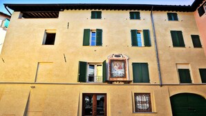 A building with a yellow facade, green shutters, and a central entrance with a door and a small balcony.