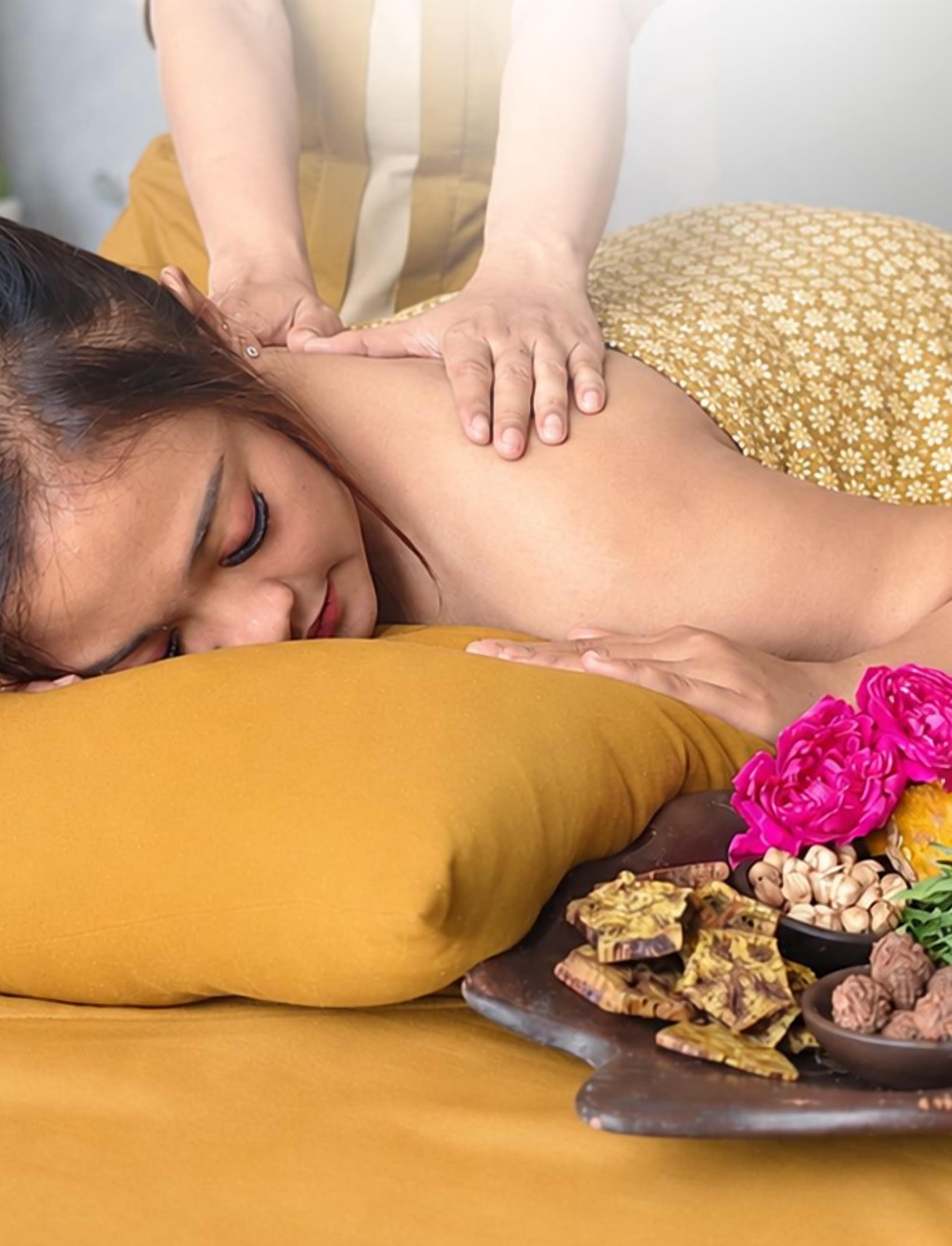 A person receiving a massage on a bed with a yellow pillow and a tray of nuts and dried flowers.