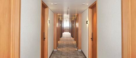 Un pasillo largo y estrecho con puertas de madera a ambos lados, que conduce a una habitación luminosa al final.