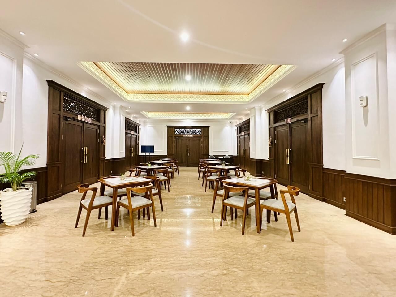 Une salle à manger d’hôtel avec de nombreuses tables et chaises, un sol en marbre poli et des lambris en bois sur les murs.