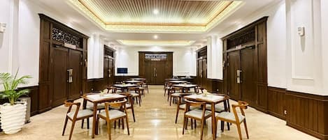 Une salle à manger d’hôtel avec de nombreuses tables et chaises, un sol en marbre poli et des lambris en bois sur les murs.