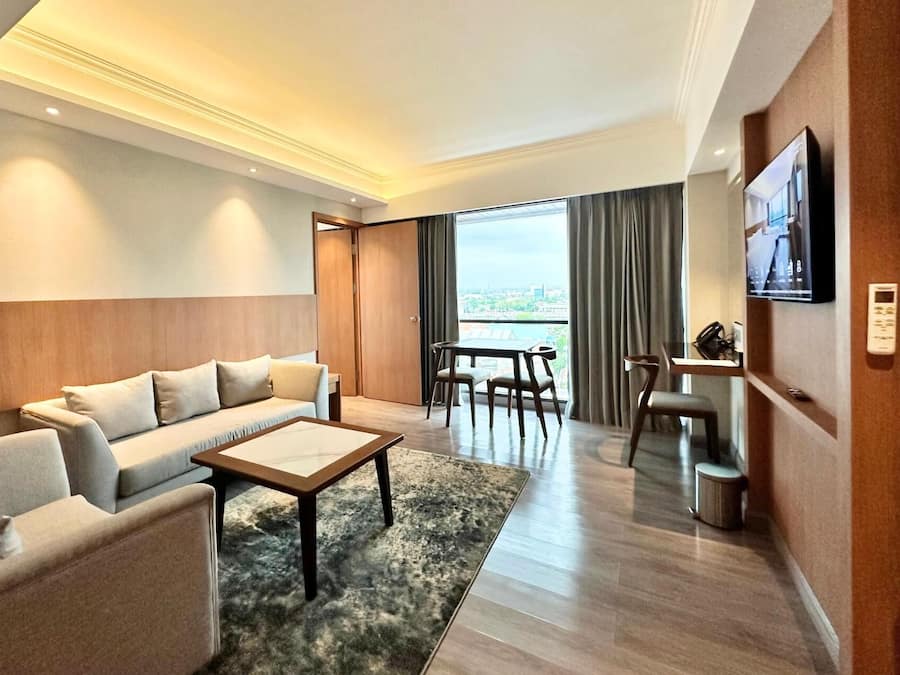 A modern hotel room with a sofa, coffee table, and dining area.