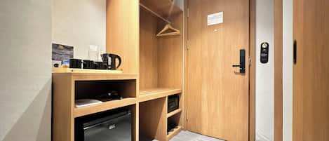 A compact hotel room with a built-in mini-fridge, a coffee maker, and a wooden wardrobe.