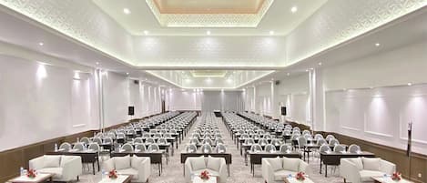 Un salón de conferencias con filas de mesas y sillas, piso alfombrado y techo con diseño.