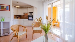 Une cuisine moderne avec des meubles blancs, un four à micro-ondes et un four traditionnel. On y trouve des chaises en osier et une table agrémentée d’un vase de plantes.