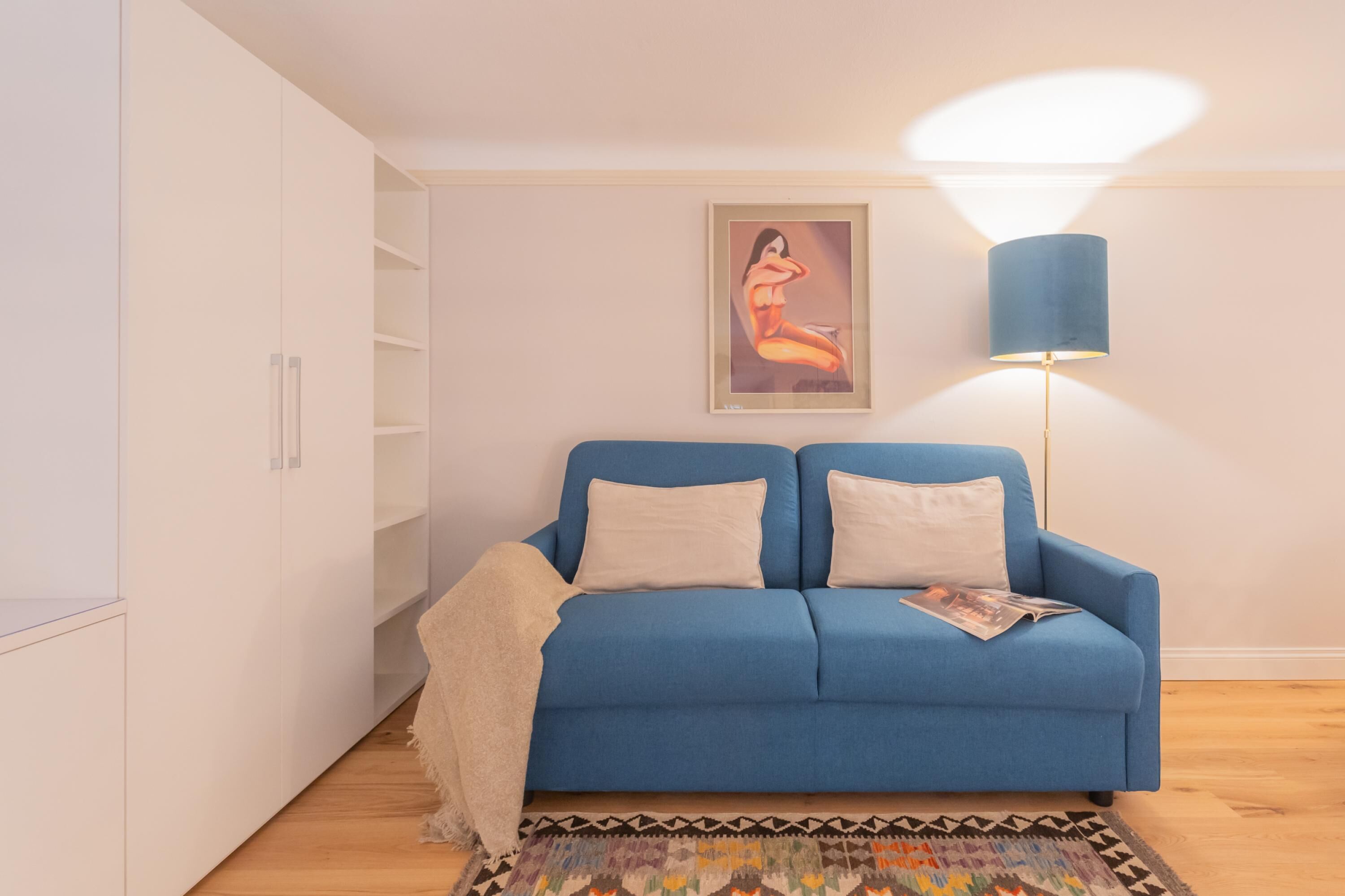 Una sala de estar moderna con un sofá azul, un tapete estampado, una lámpara de pie y una obra de arte enmarcada en la pared.