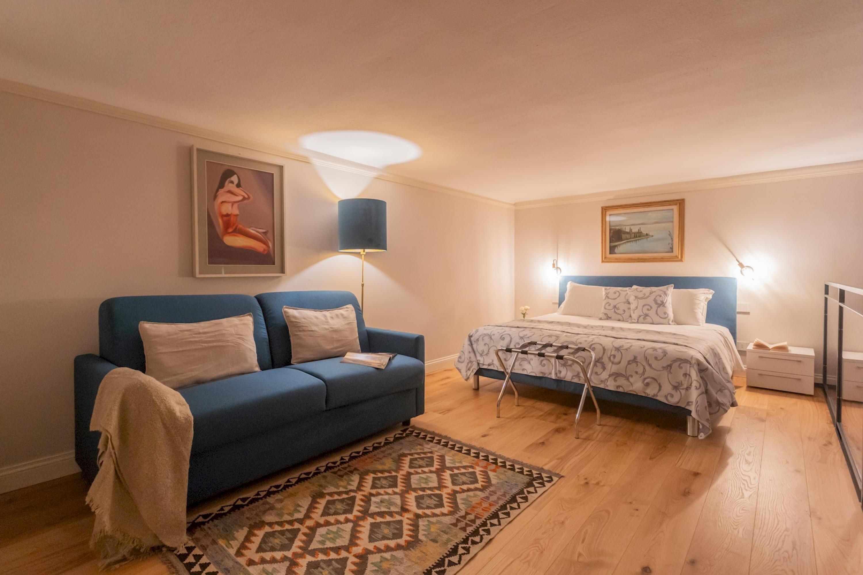 Una camera da letto con un divano blu, un letto con copriletto decorato, un tappeto e un quadro appeso al muro.